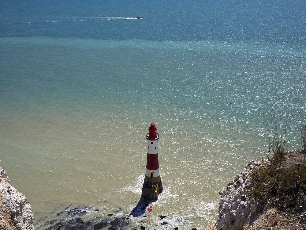 Beachy Head Lighthouse seen from the coast path above with glittering sea and a speedboat on a sunny day, East Sussex, UK, East Sussex, England