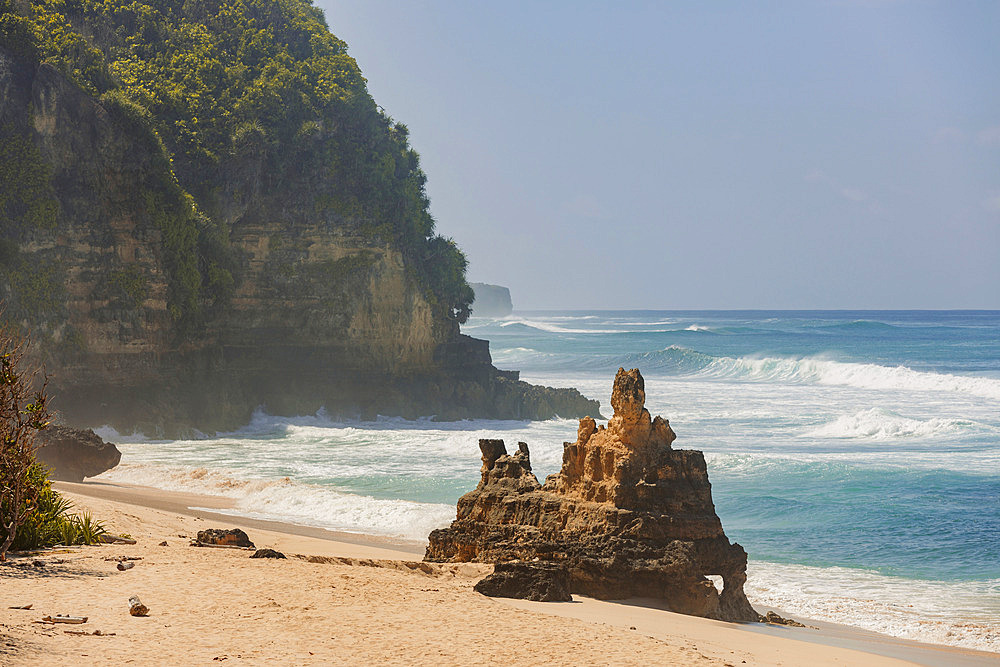 Beautiful scenic view of Mbawana Beach with crashing waves along the sea cliffs and rock formations on the sand at the water's edge, Kodi Bangedo, Southwest Sumba Regency, East Nusa Tenggara, Indonesia