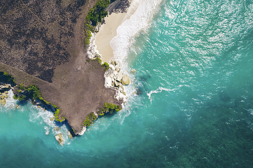 Aerial view of barren land above Mbawana Beach, with surf and turquoise ocean water rolling into the white sand beach below, East Nusa Tenggara, Indonesia, Kodi Bangedo, Southwest Sumba Regency, East Nusa Tenggara, Indonesia