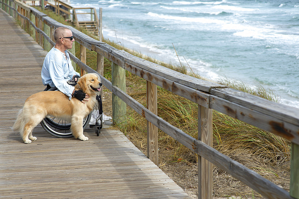 Paraplegic man in wheelchair with service dog enjoys the ocean view from a boardwalk, Boynton Beach, Florida, United States of America