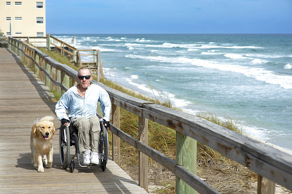 Paraplegic man in wheelchair with service dog enjoys the ocean view from a boardwalk, Boynton Beach, Florida, United States of America