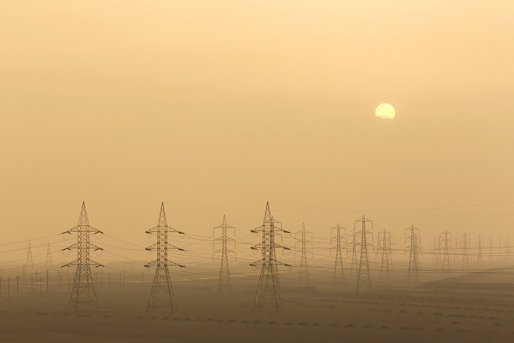 Power pylons stretch into the distance, sun rises through air thick with sand, Suez Canal, Port Said, Egypt, North Africa