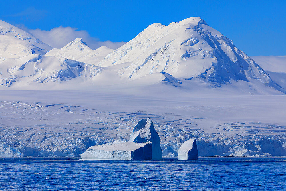 Non-tabular iceberg off glaciated, mountainous Anvers Island, blue sky, Antarctic Peninsula, Antarctica, Polar Regions