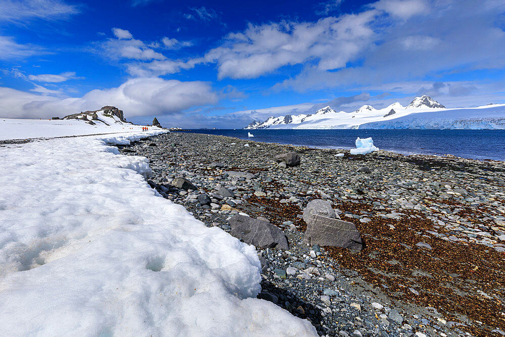 Expedition tourists walk on shore of Half Moon Island, view to Livingston Island, blue sky, South Shetland Islands, Antarctica, Polar Regions