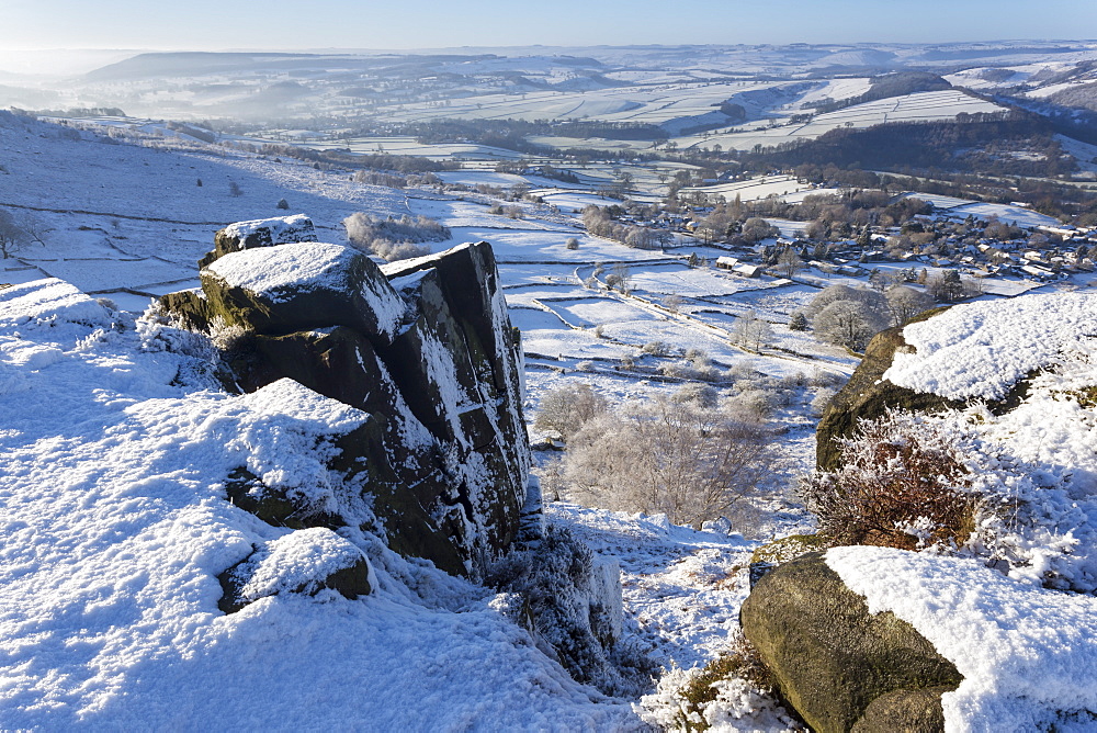 Snowy Curbar village beyond the rocks of Curbar Edge, winter morning, Peak District National Park, Derbyshire, England, United Kingdom, Europe