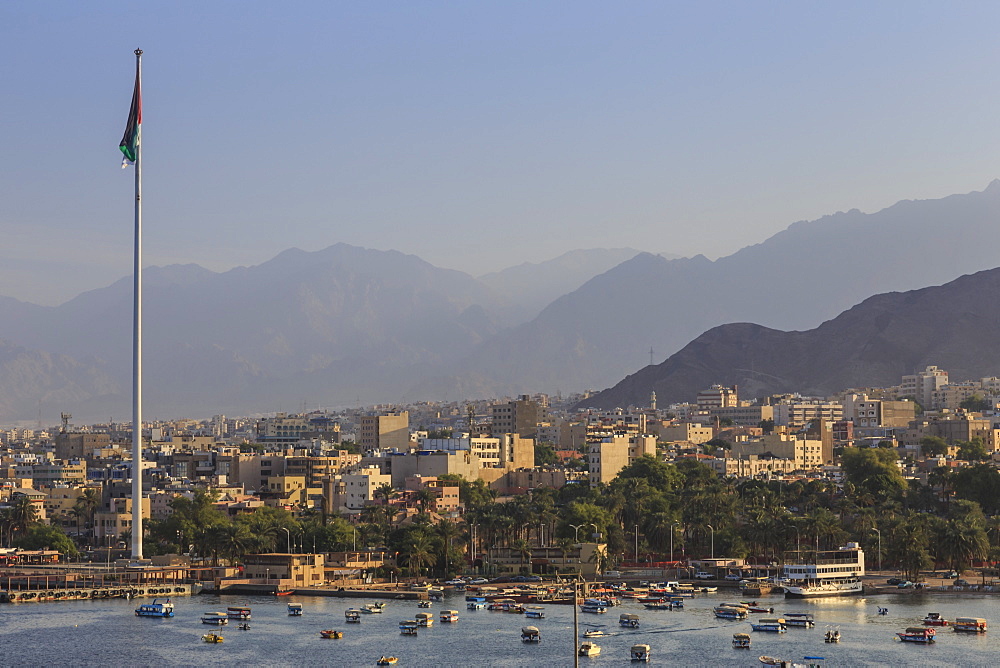 Elevated view of Aqaba seafront with huge Jordanian flag, boats and hazy mountains in distance, Aqaba, Jordan, Middle East