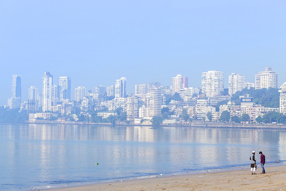 A Muslim and a Hindu man talking on Chowpatty beach with the skyscrapers of wealthy Malabar Hill behind, Mumbai, Maharashtra, India, Asia