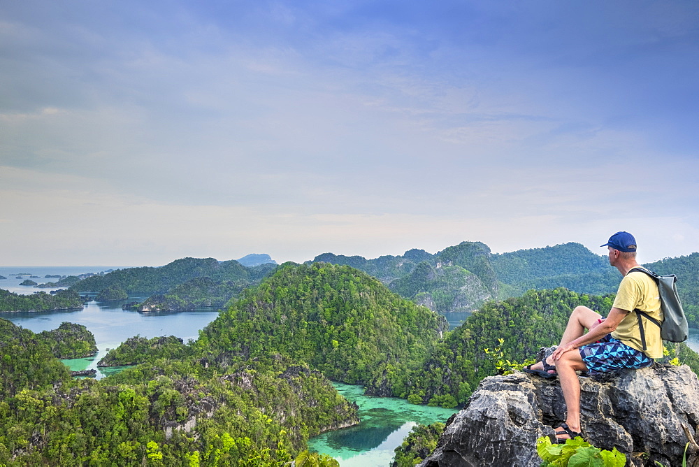 A tourist looking out over a bay of islands from Harfat mountain, Spice Islands, West Papua, Indonesia, Southeast Asia, Asia