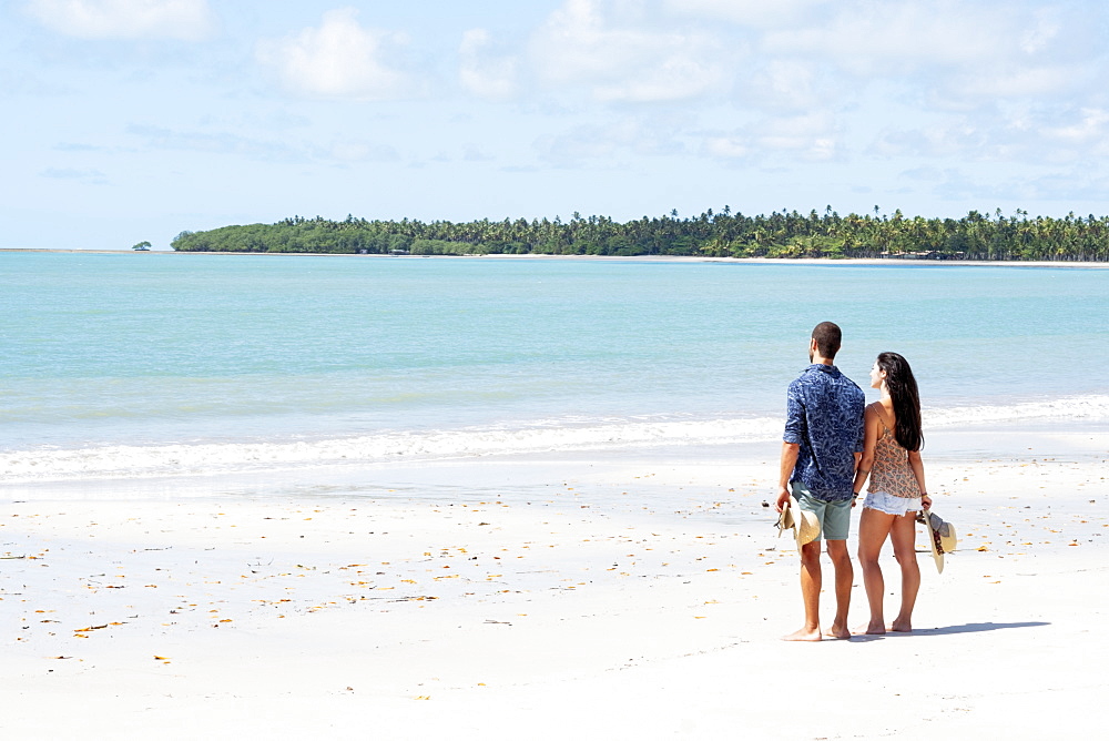 A good-looking Hispanic (Latin) couple on a deserted beach with backs to camera, Brazil, South America