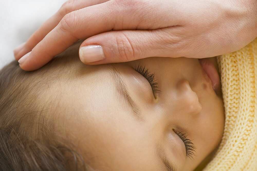 Close up of Hispanic sleeping baby with mother's hand on cheek