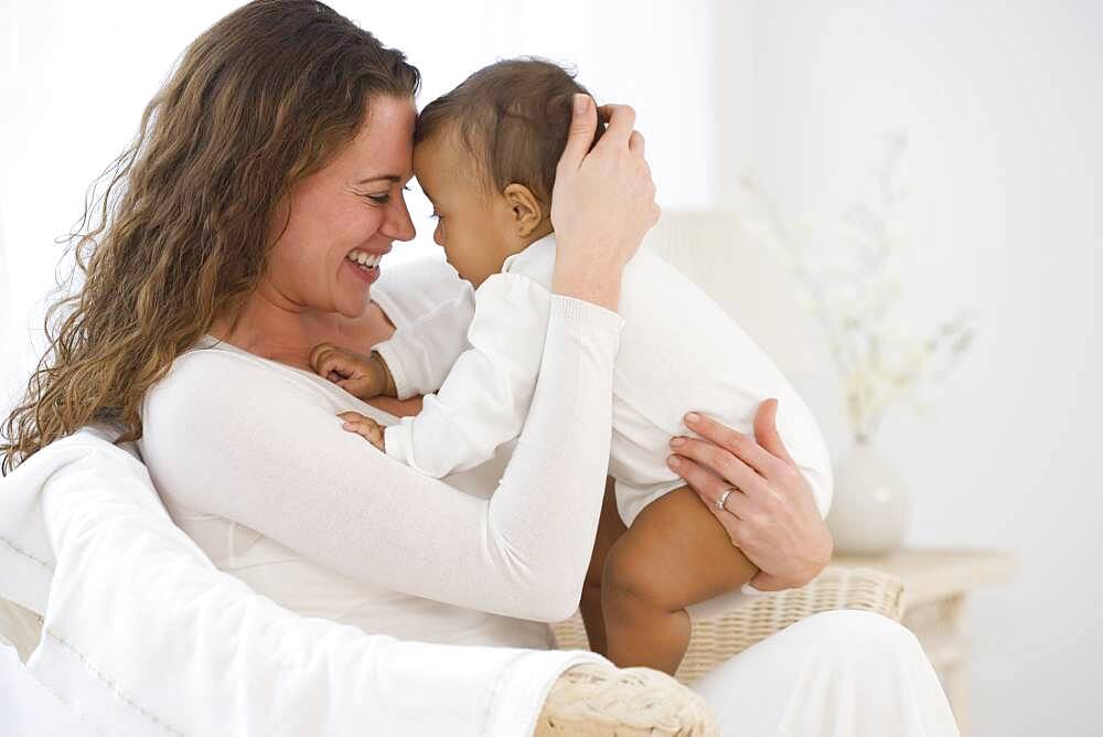 Hispanic mother sitting in chair hugging baby