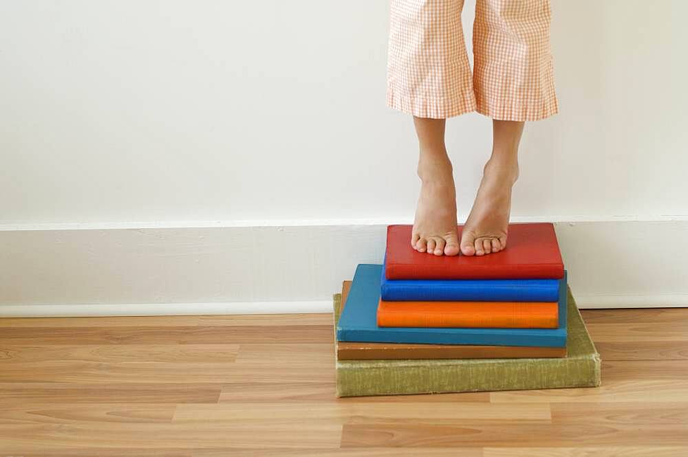 Girl standing on tiptoes on stack of books