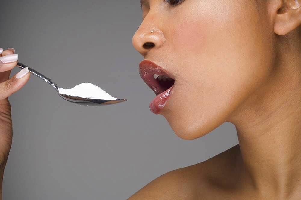 African woman eating spoon of sugar