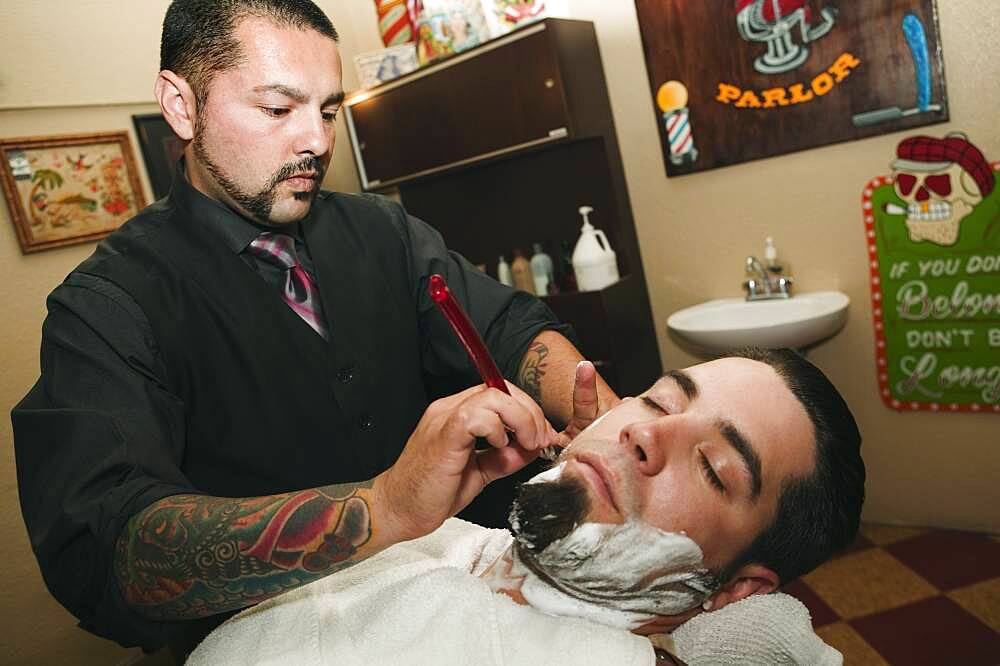 Hispanic barber shaving man's face