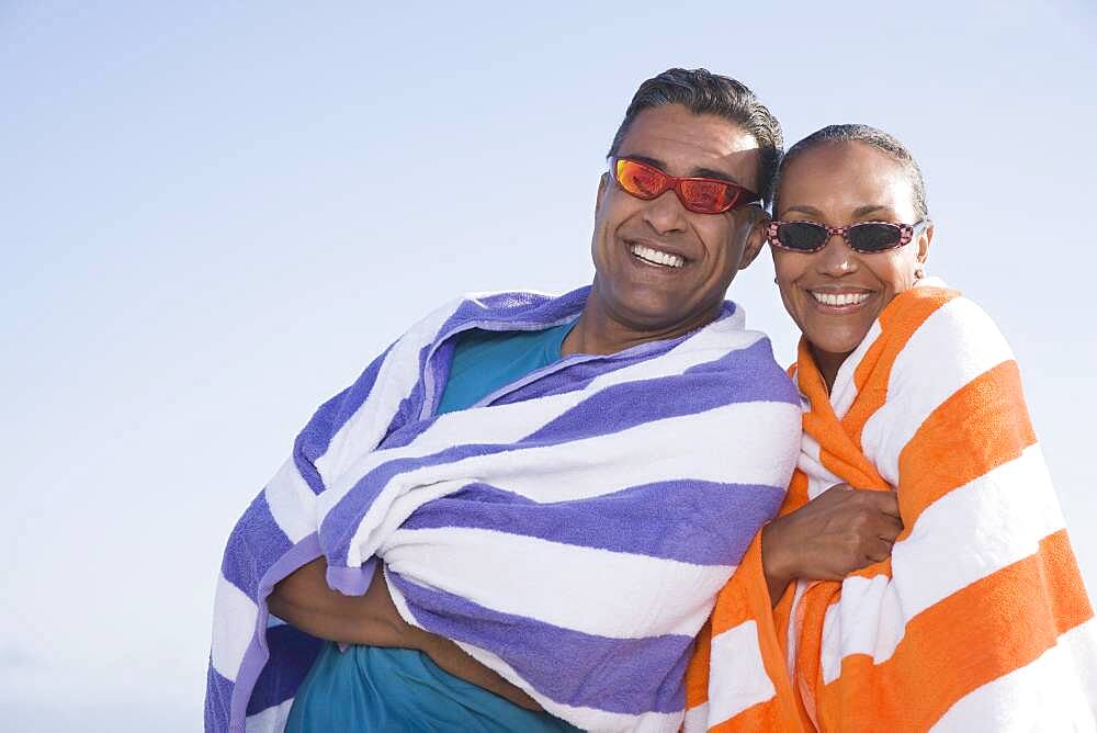 Multi-ethnic couple wrapped in beach towels