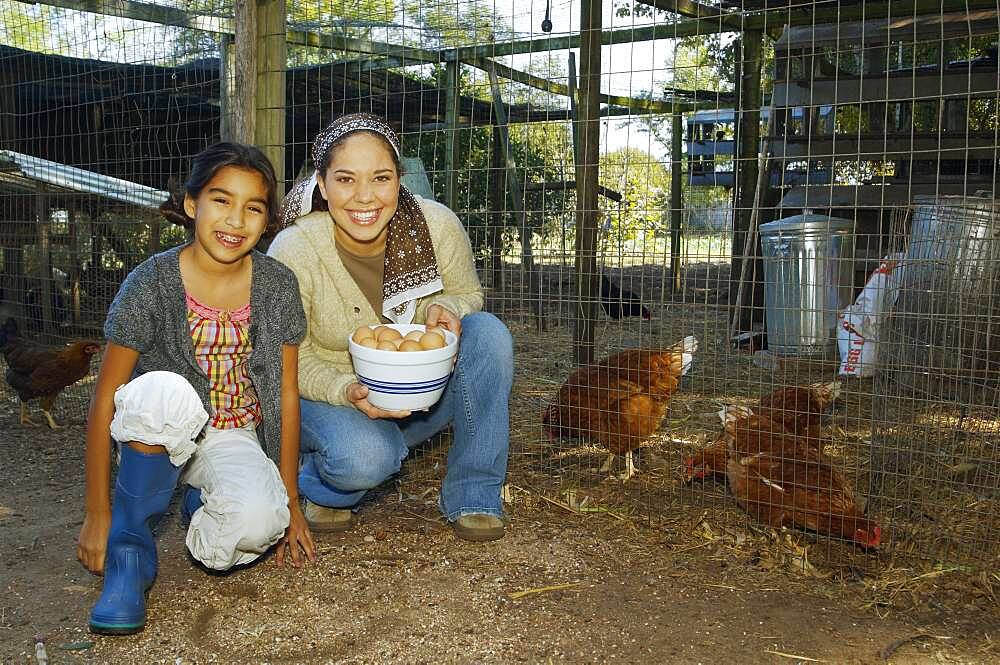 Hispanic mother and daughter with bowl of eggs next to chickens