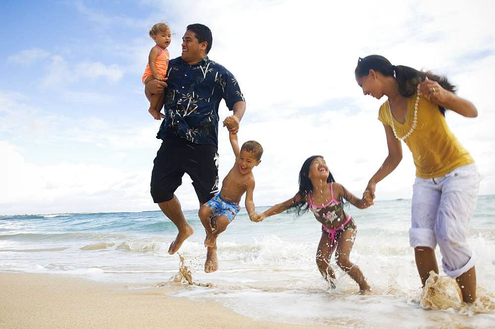 Pacific Islander family jumping in ocean surf