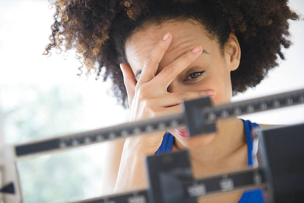 Mixed race woman hiding from weight on scale