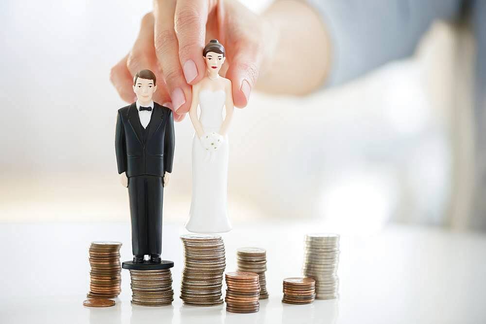 Mixed race woman balancing bride and groom statues on coin stacks