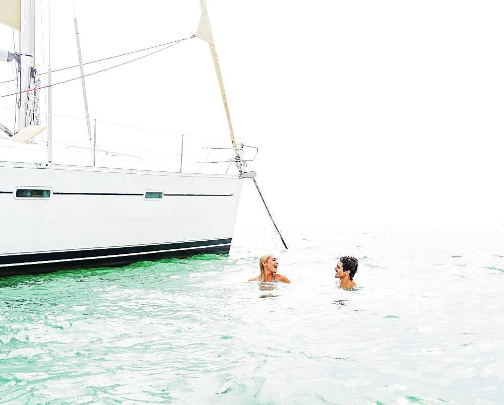 Couple swimming near sailboat