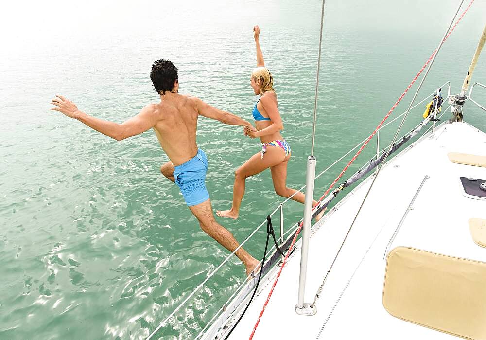 Couple jumping from sailboat deck into ocean