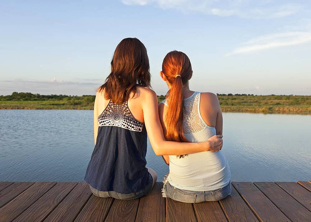 Caucasian women sitting on wooden dock over lake