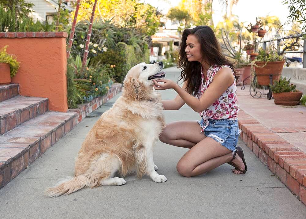 Mixed race woman petting dog on sidewalk