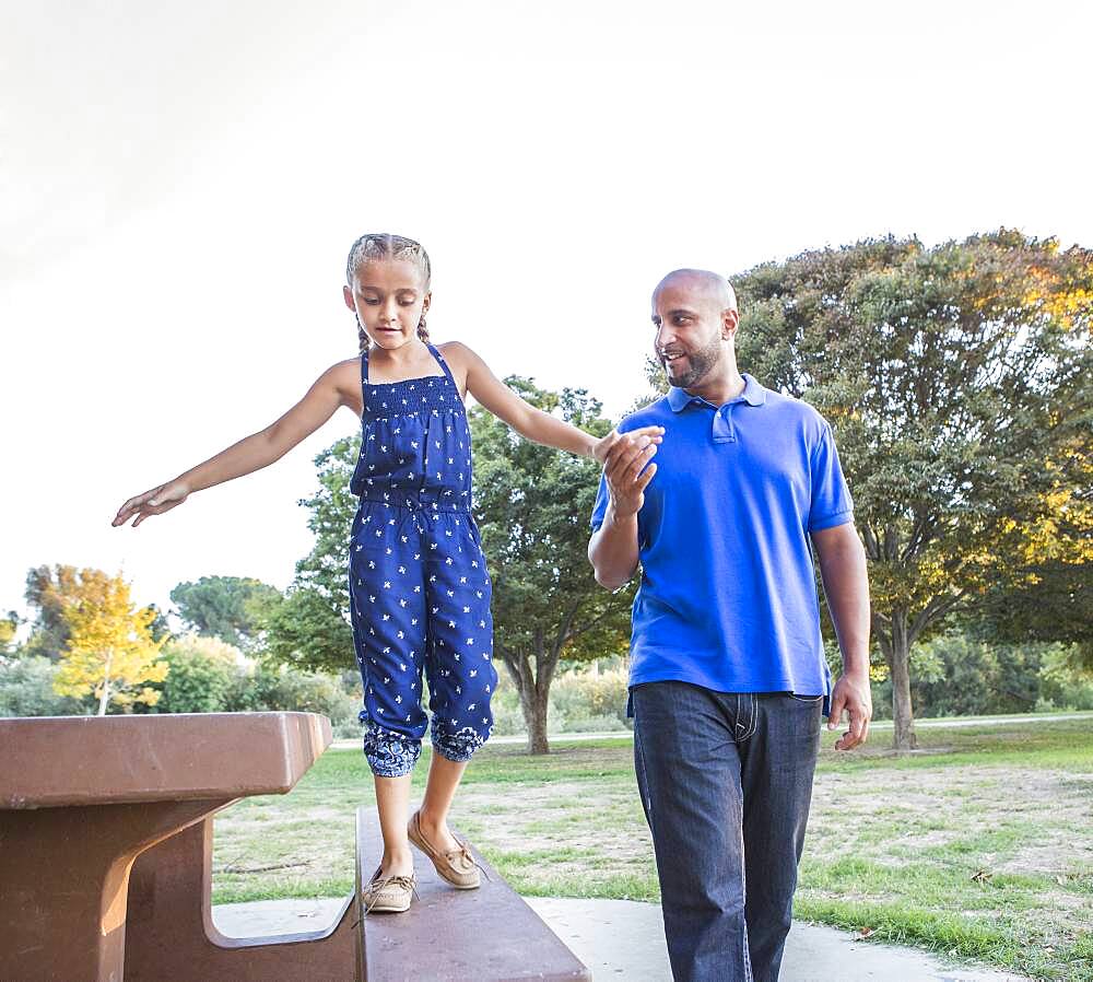 Father and daughter playing on picnic table in park