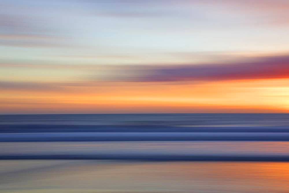 Defocused view of ocean waves on beach under sunset sky