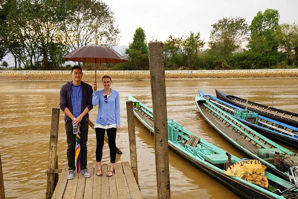 Couple standing under umbrella on wooden dock