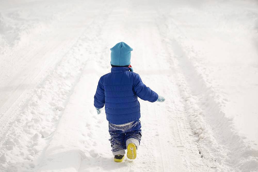 Caucasian boy walking in tire tracks in snow