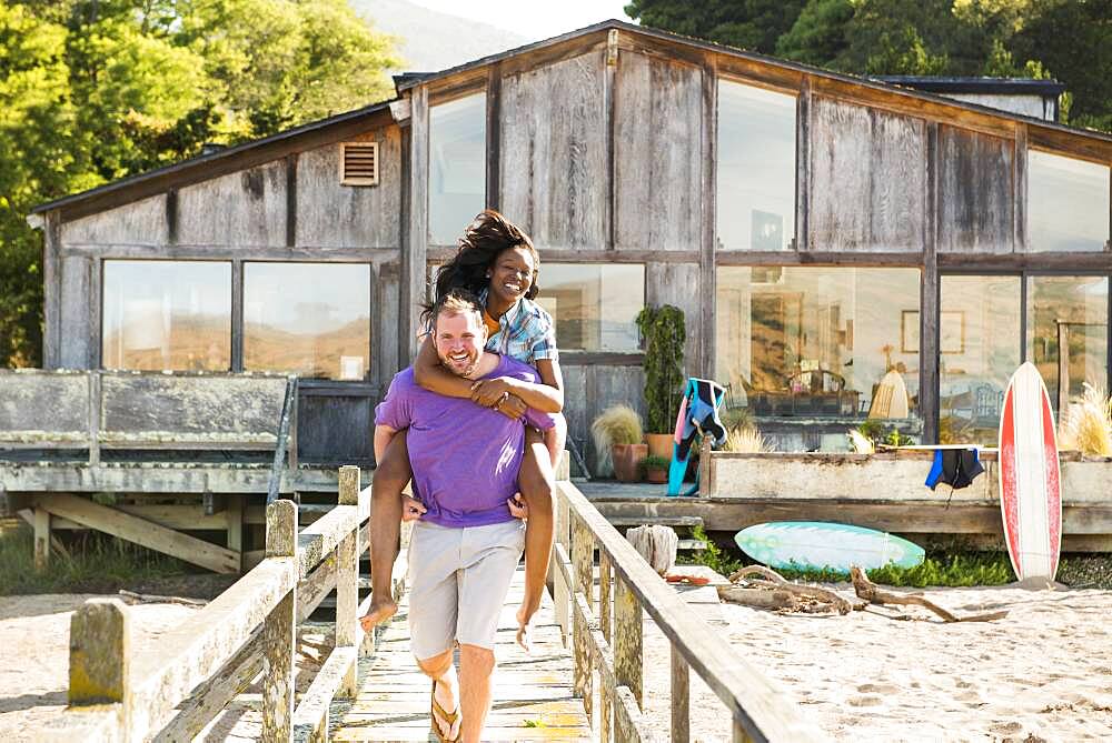 Man carrying girlfriend piggyback on wooden deck