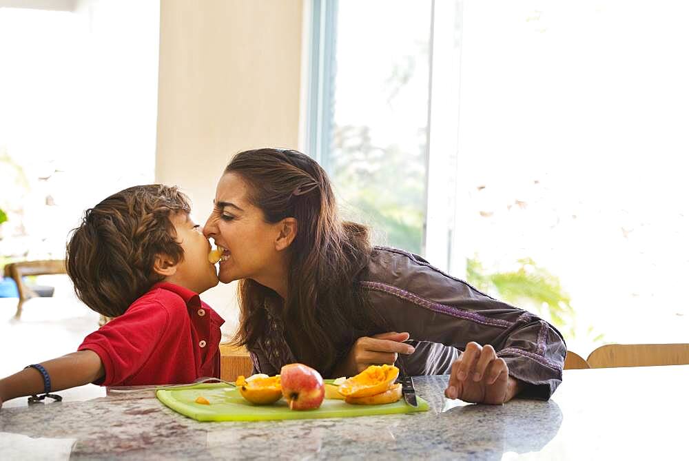 Hispanic mother and son eating fruit in kitchen