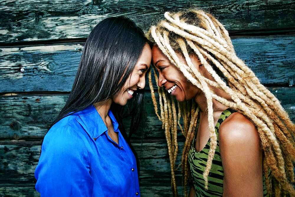 Smiling women touching foreheads at wooden wall