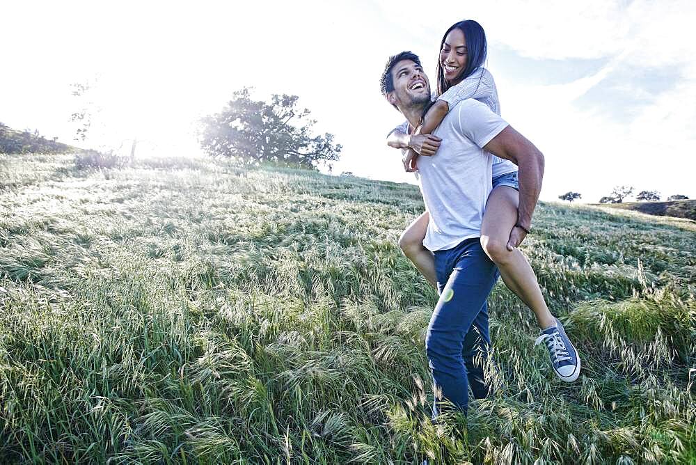 Man carrying girlfriend piggyback in field