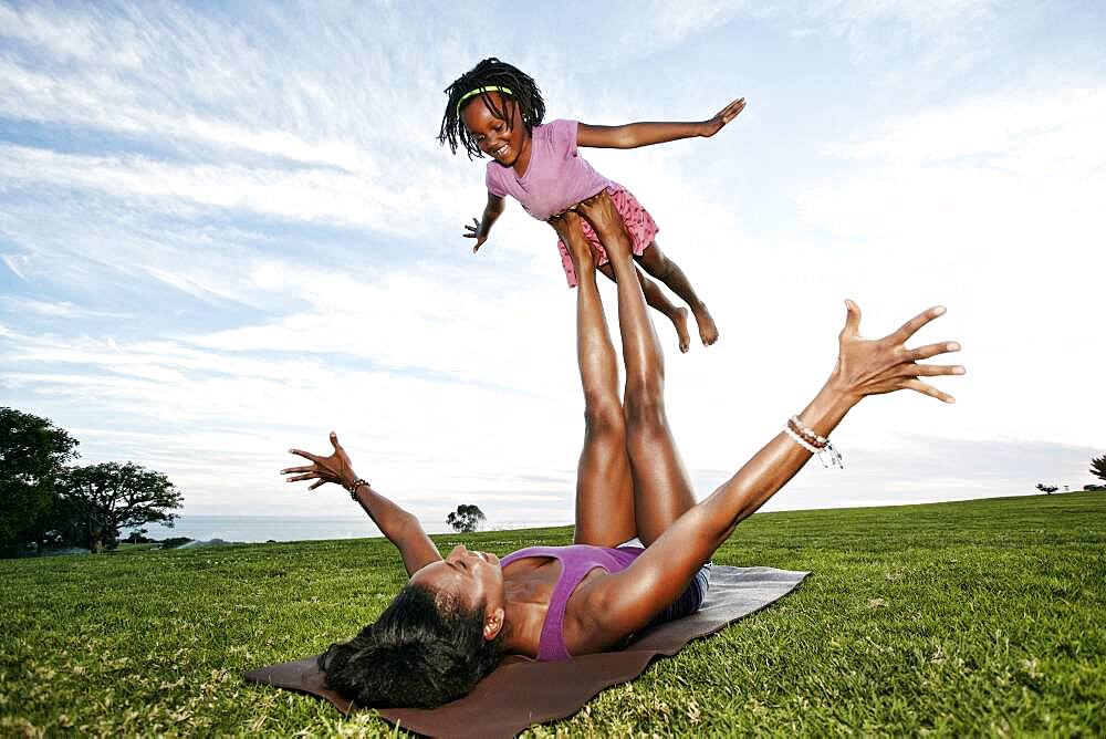 Mother balancing daughter on legs in park