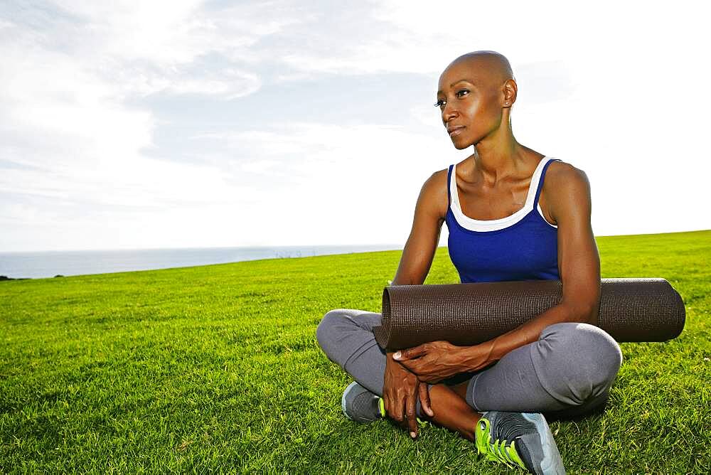 African American woman holding yoga mat in park