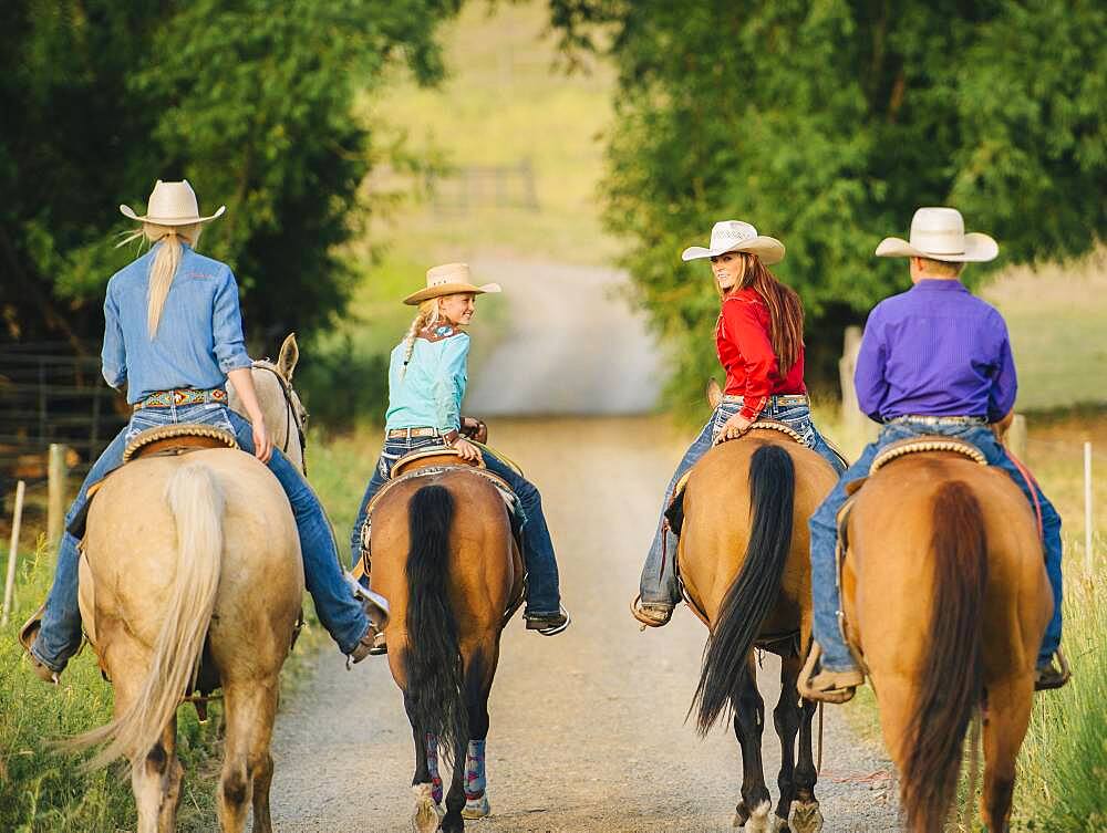 Cowgirls and cowboy riding horses in rural road