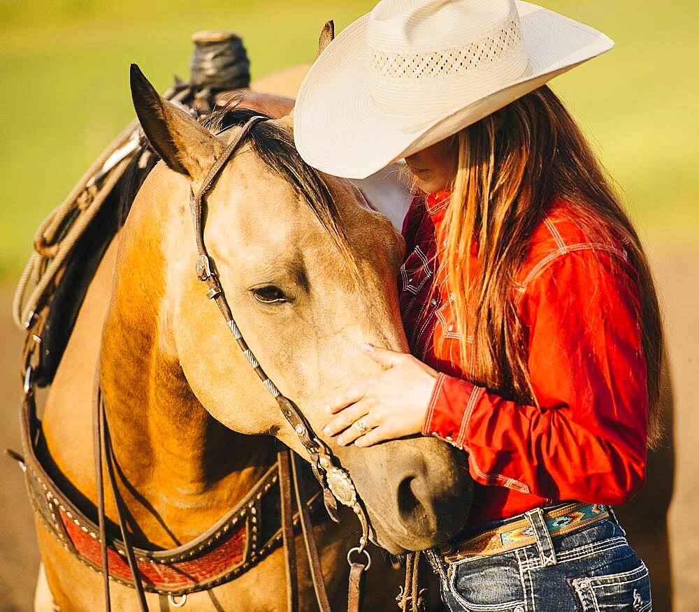 Caucasian cowgirl petting horse on ranch