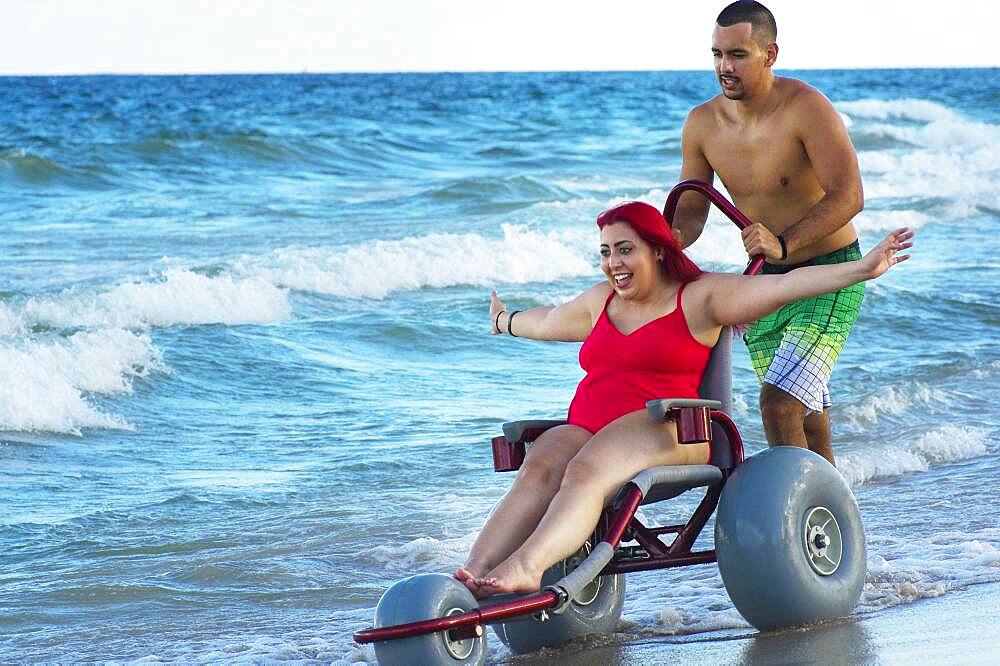 Man pushing paraplegic girlfriend in wheelchair on beach