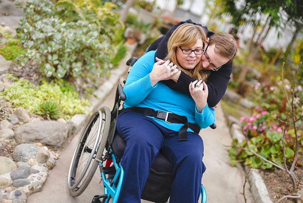 Man hugging paraplegic girlfriend in garden