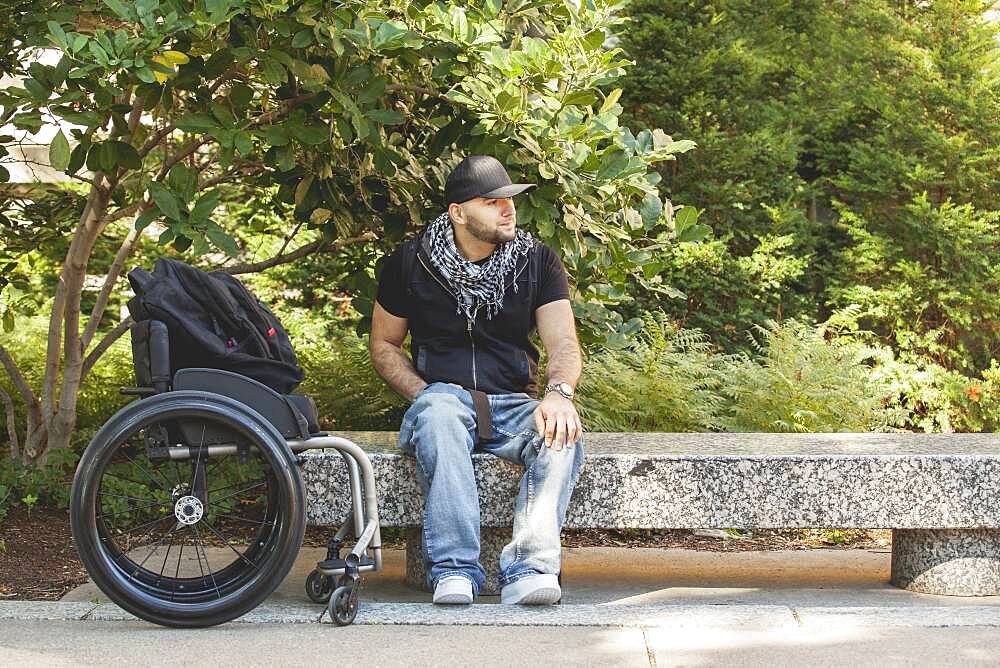 Disabled man and wheelchair sitting on stone bench