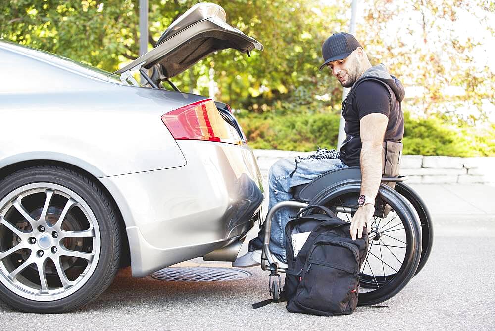 Disabled man in wheelchair packing car trunk