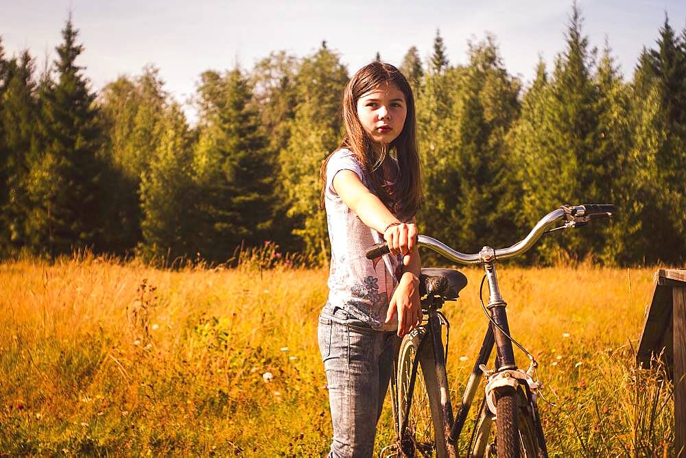 Caucasian teenage girl pushing bicycle in field