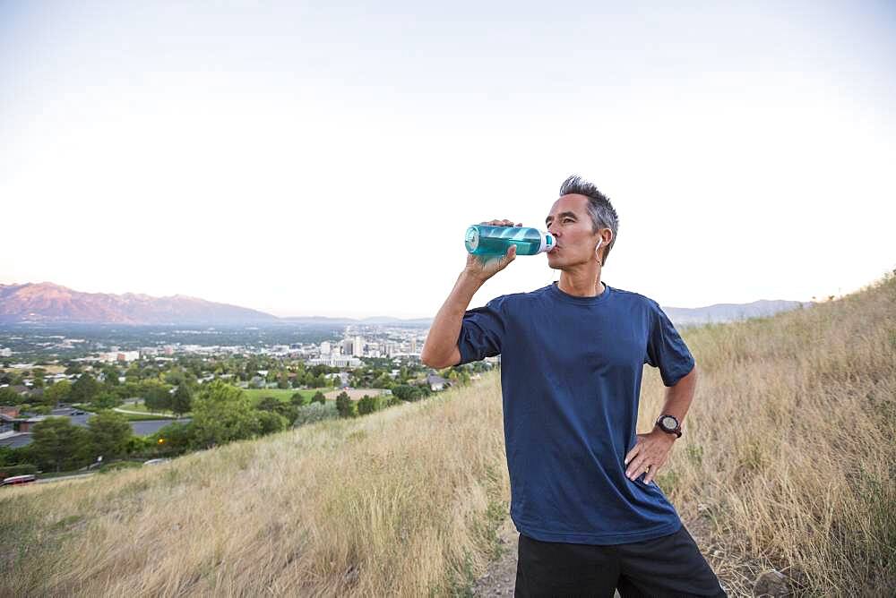 Mixed race man drinking water bottle on hilltop