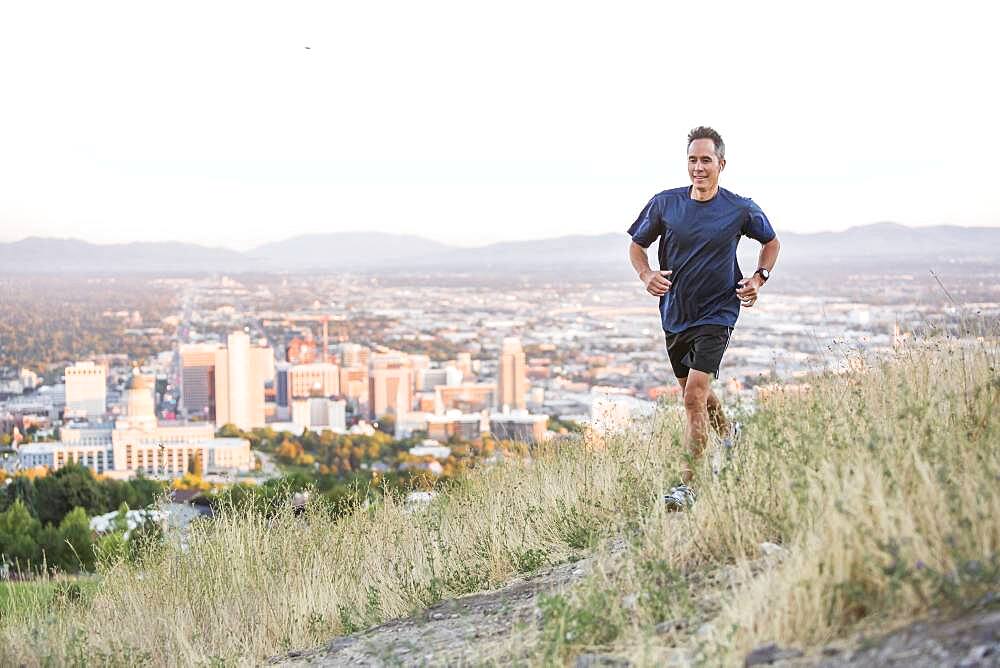 Mixed race man running on hilltop over Salt Lake City, Utah, United States