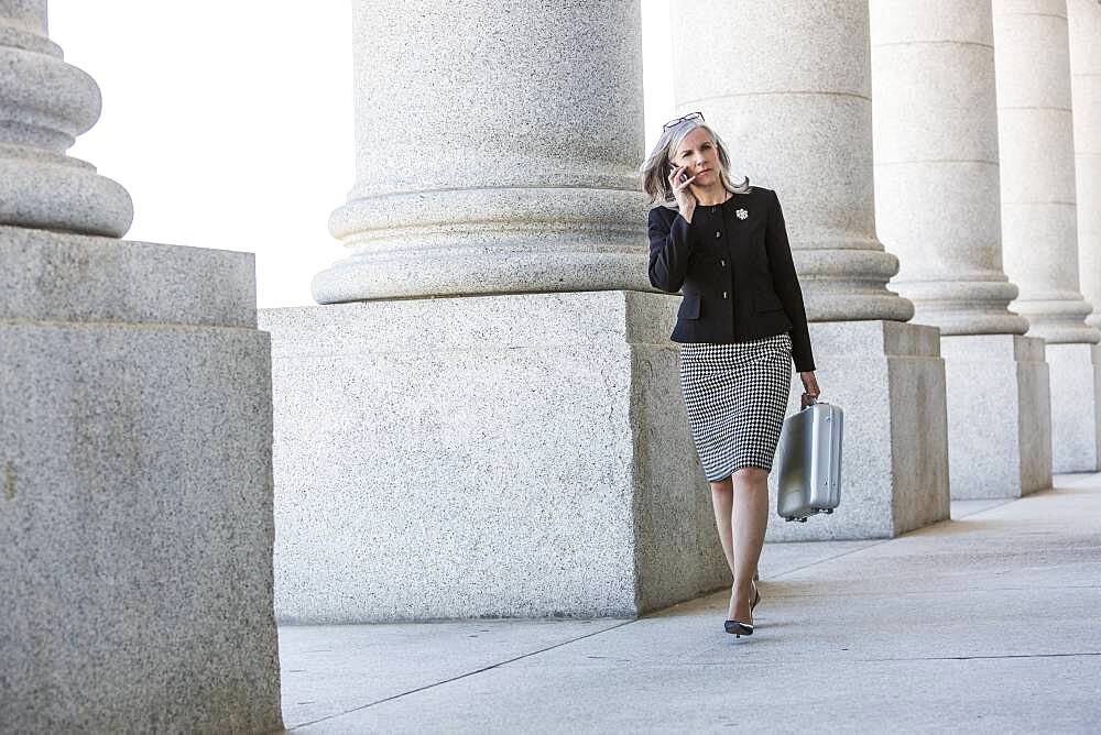 Caucasian businesswoman talking on cell phone under columns