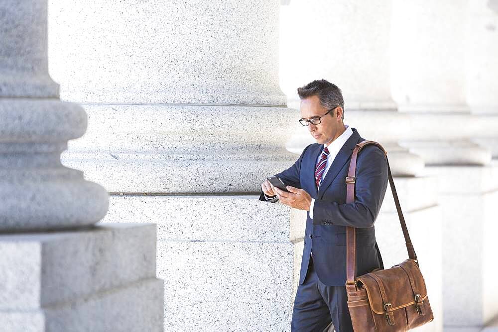 Mixed race businessman using cell phone under columns