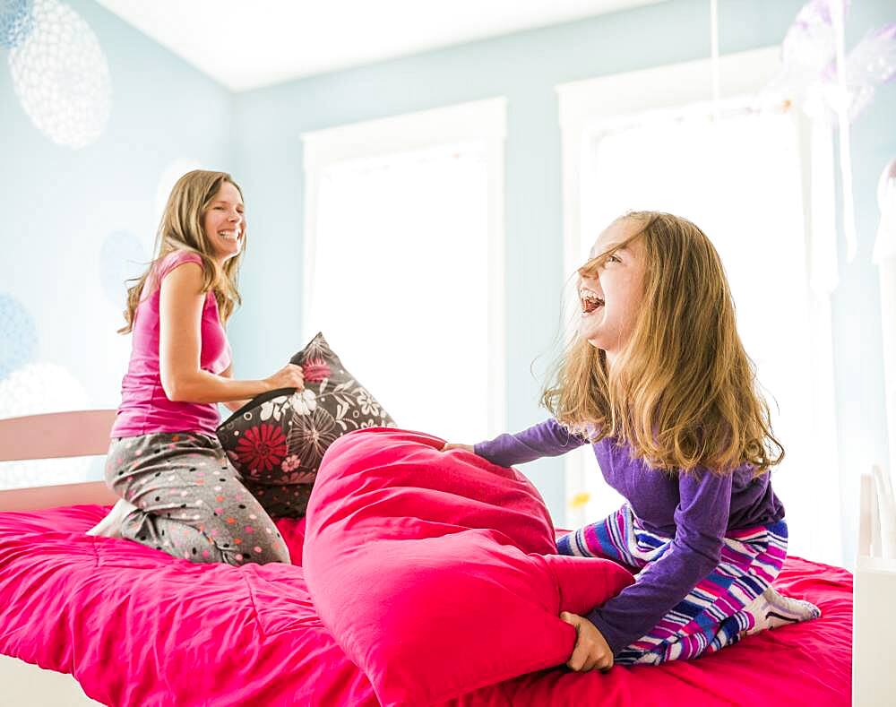 Caucasian mother and daughter having pillow fight on bed