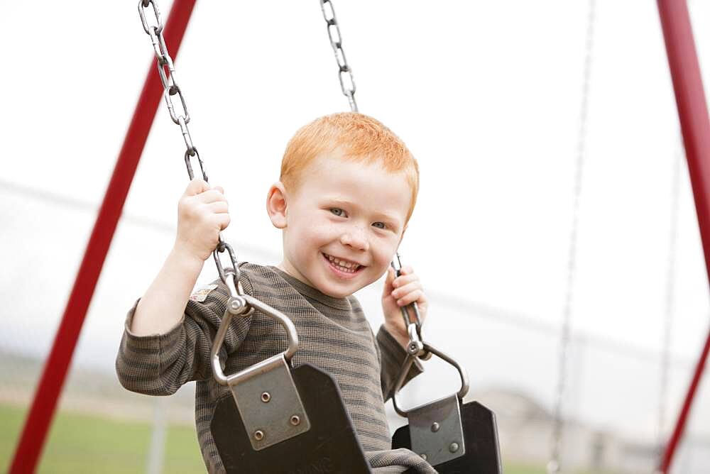 Caucasian boy sitting on playground swing